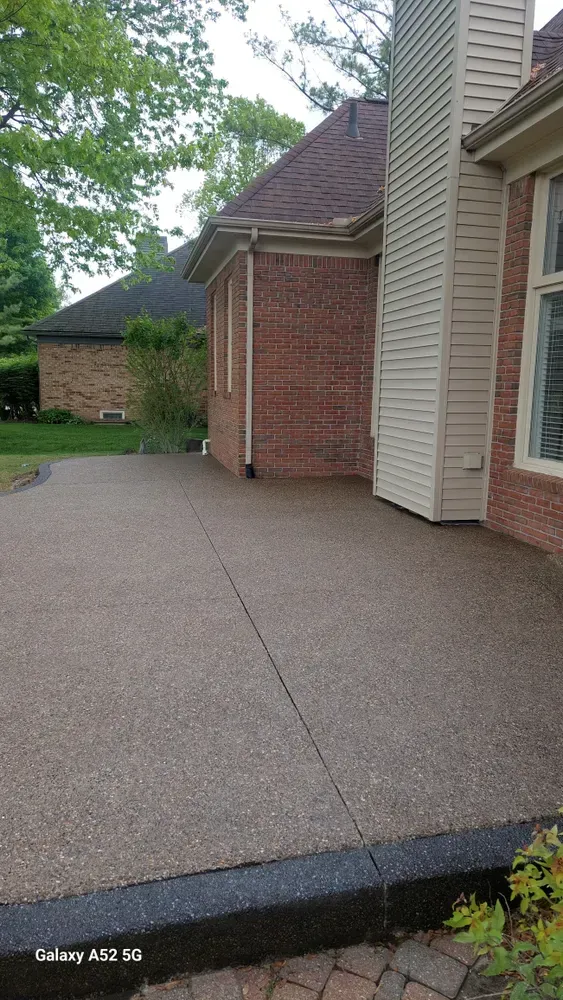 Patio next to a red brick house with a concrete surface. The patio has a black border and tan concrete.
