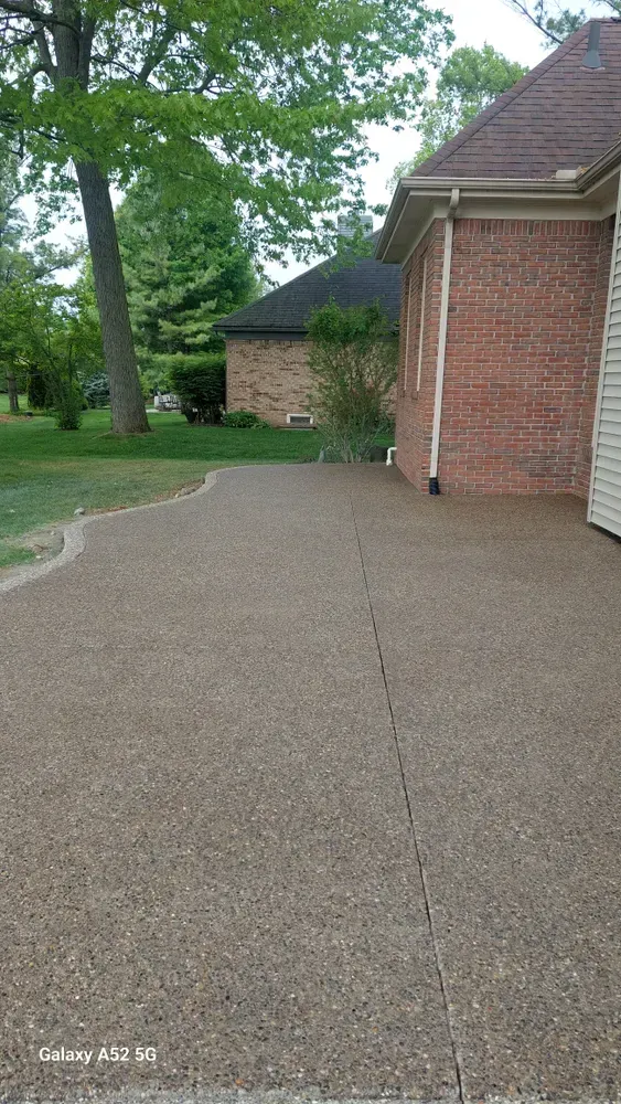 A concrete patio beside a brick house and green lawn with trees in the background.