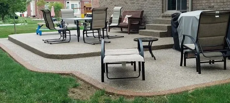 Patio with chairs and table on a raised concrete surface, surrounded by green grass.
