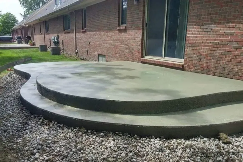 Concrete patio with steps, next to a brick building with sliding glass door and gravel landscaping.