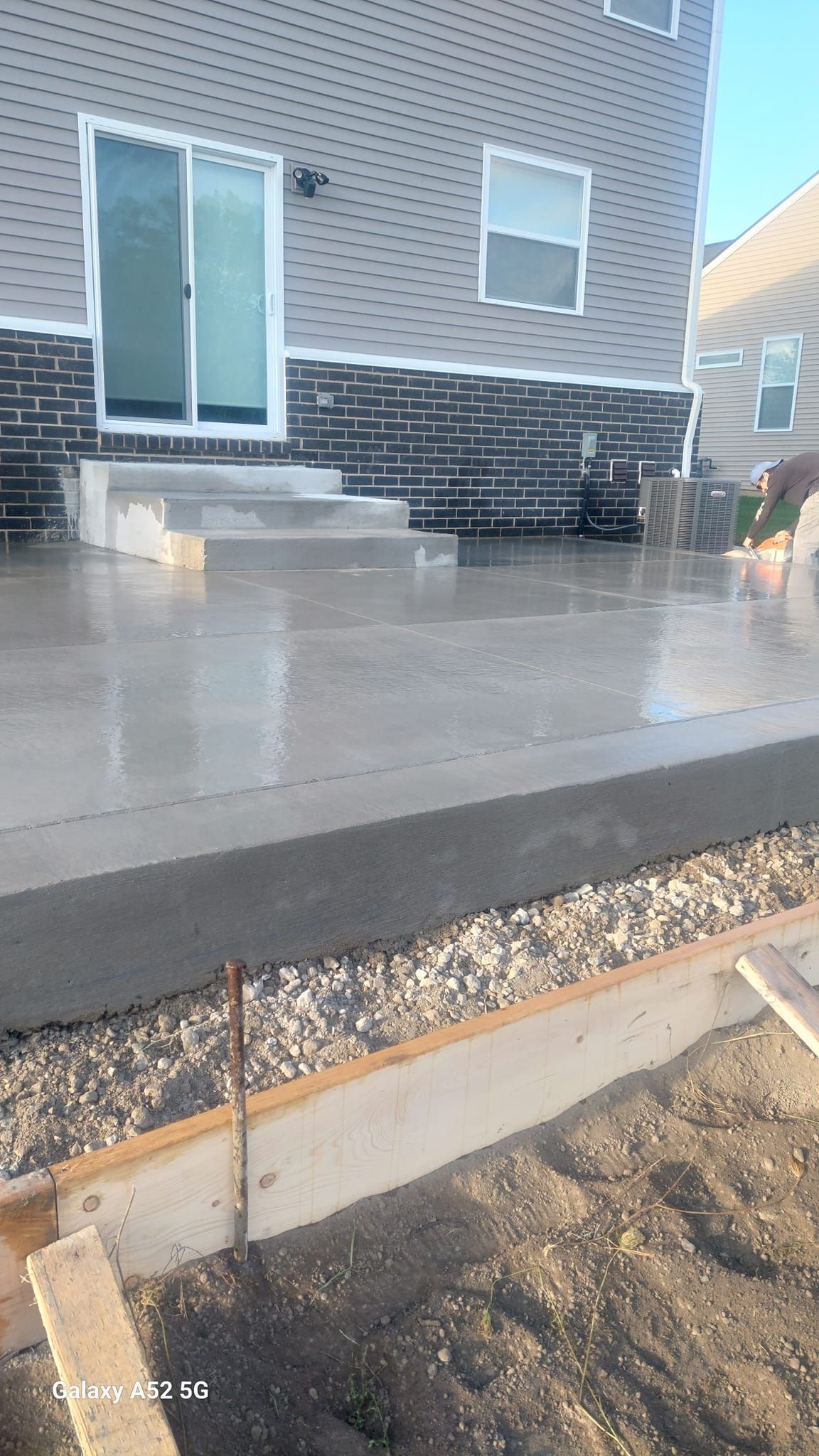 New concrete patio under construction outside a house; gray, unfinished with tools.
