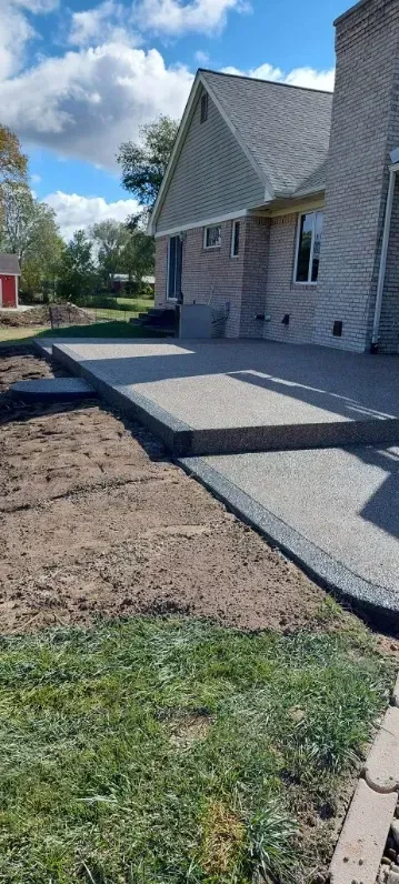 Concrete patio with steps, bordered by grass and the side of a house.