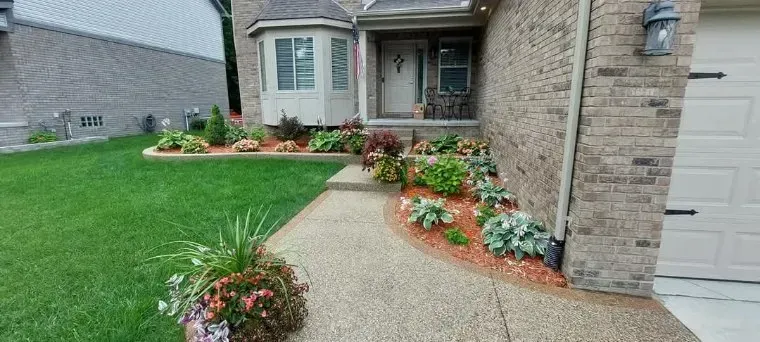 A house with a brick exterior and well-kept flowerbeds. A paved path leads to the front door.