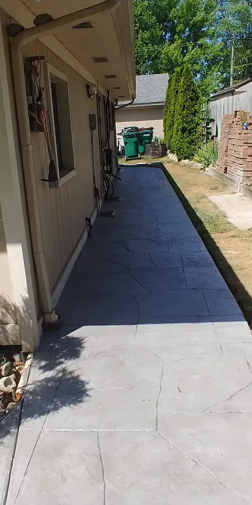 A concrete walkway alongside a beige building with a green dumpster in the background.