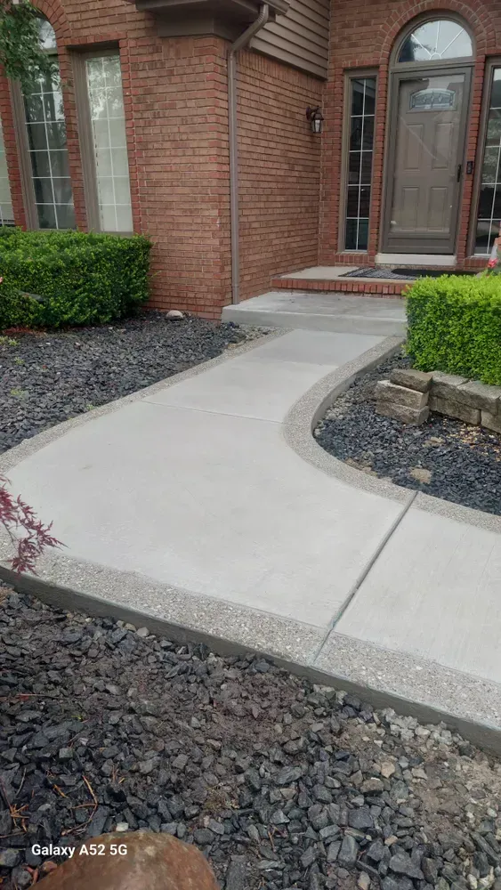 Concrete walkway with gravel border leading to a brick house's front door.