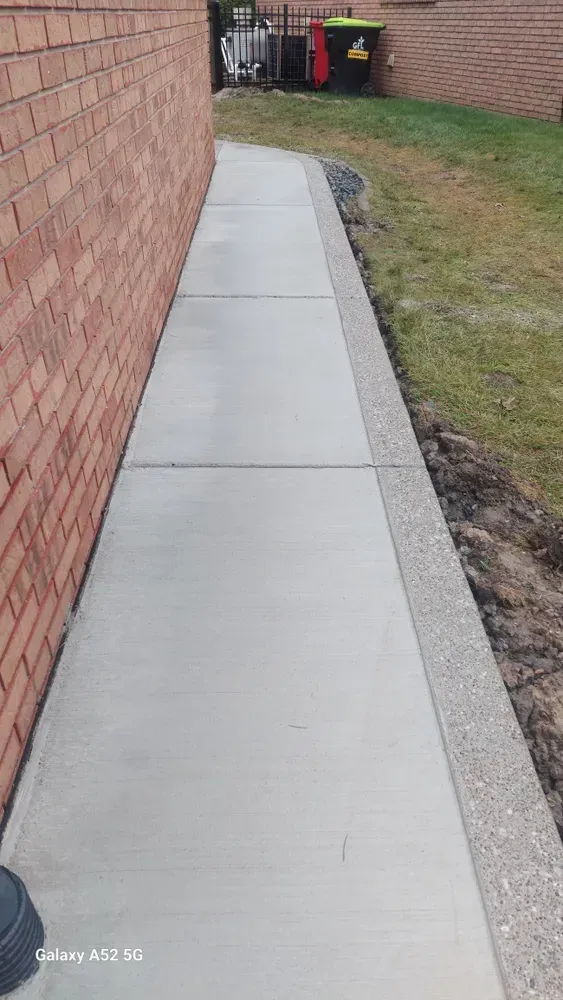 Concrete walkway beside a red brick wall and a landscaped grass area.