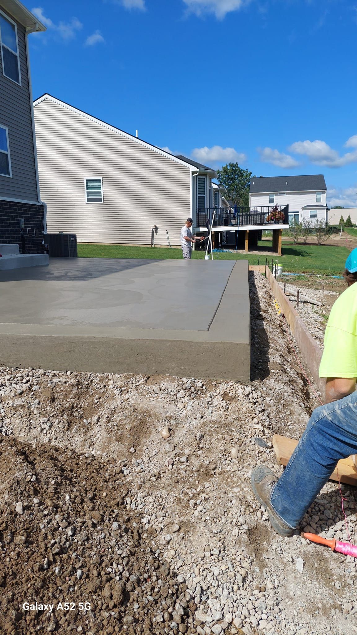 Construction worker laying concrete patio in a residential yard on a sunny day.