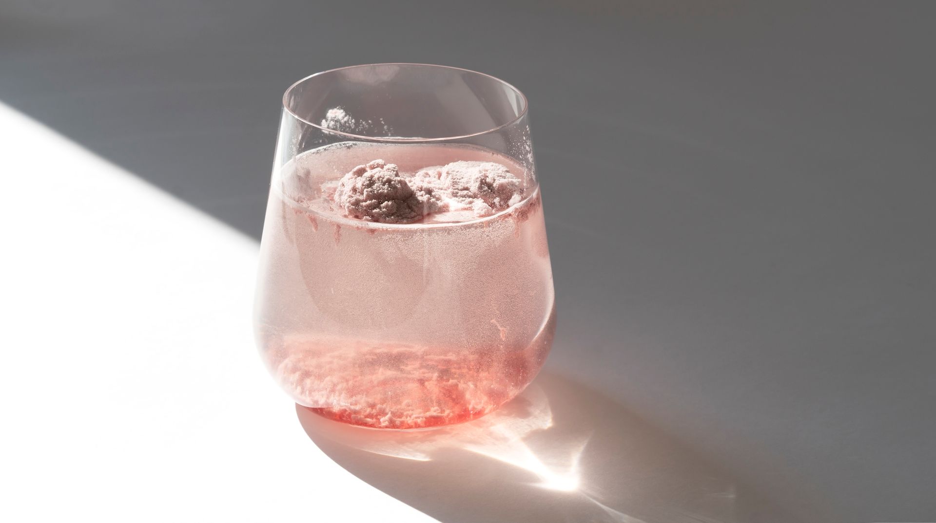 A glass of pink liquid with ice cubes in it is on a table.