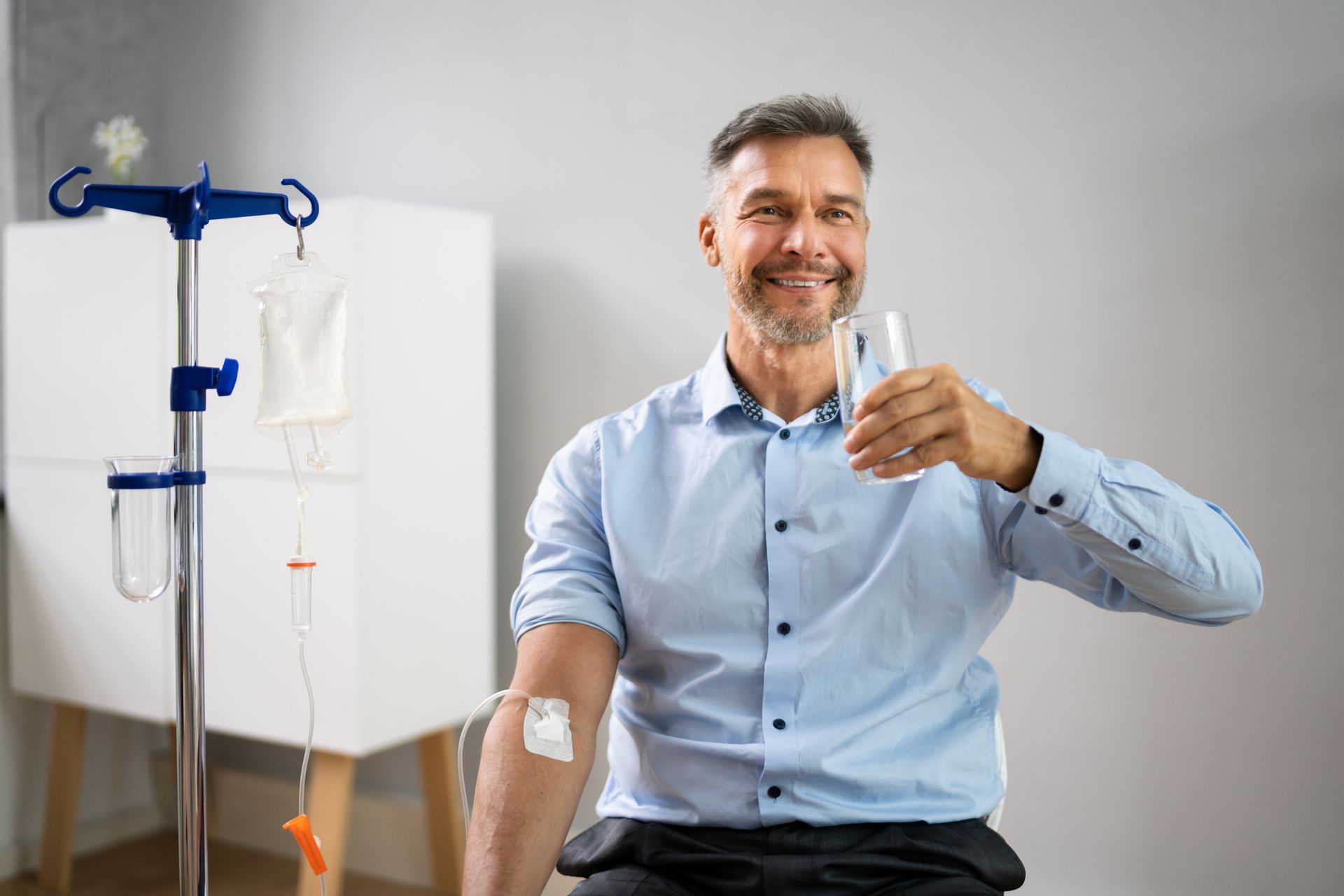 A man is sitting in a chair with an iv in his arm and drinking a glass of water.