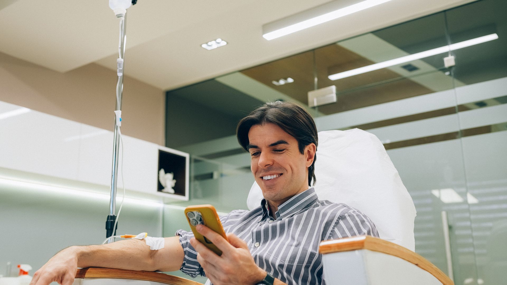 A man is sitting in a hospital bed using a cell phone.