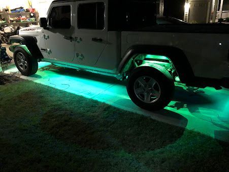 A white jeep is parked in a grassy area with green lights.