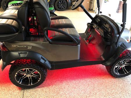 A golf cart is parked in a garage with red lights on the wheels.