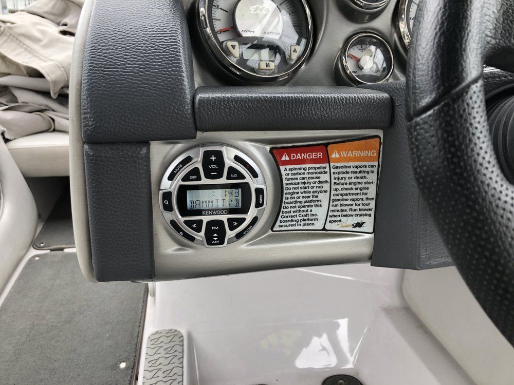 The dashboard of a boat has a radio and a steering wheel.
