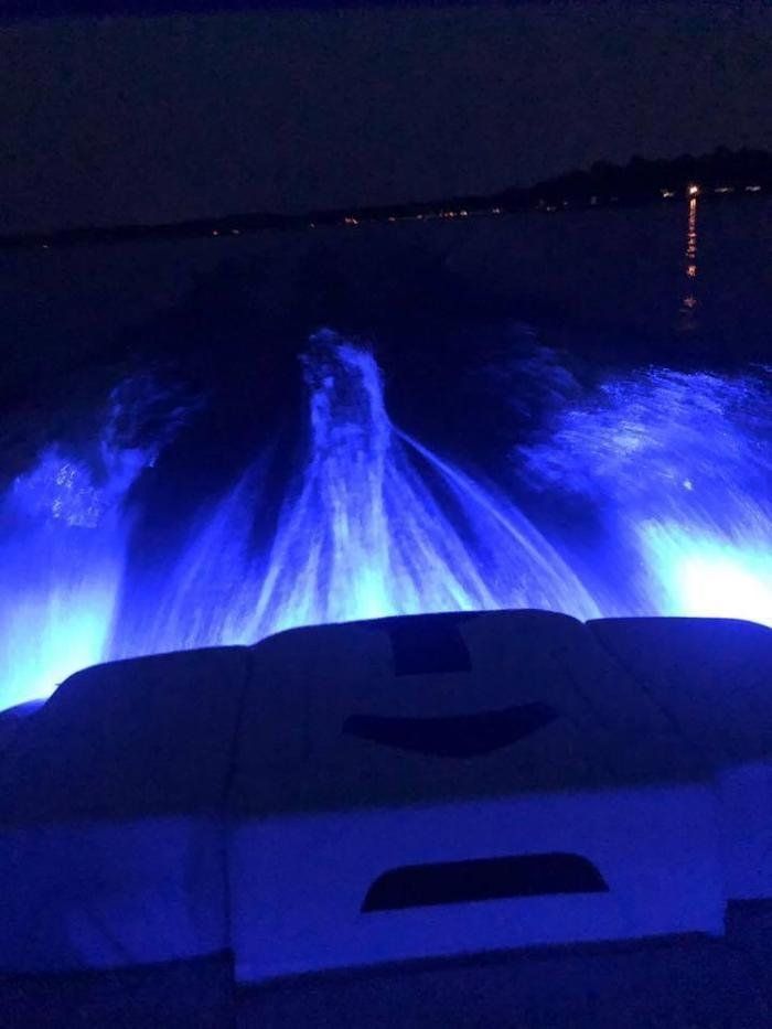 The back of a boat is lit up with blue lights at night.
