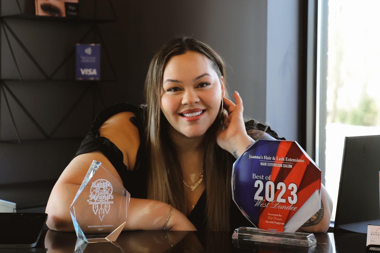 A woman is sitting at a table holding a trophy with the year 2023 on it.