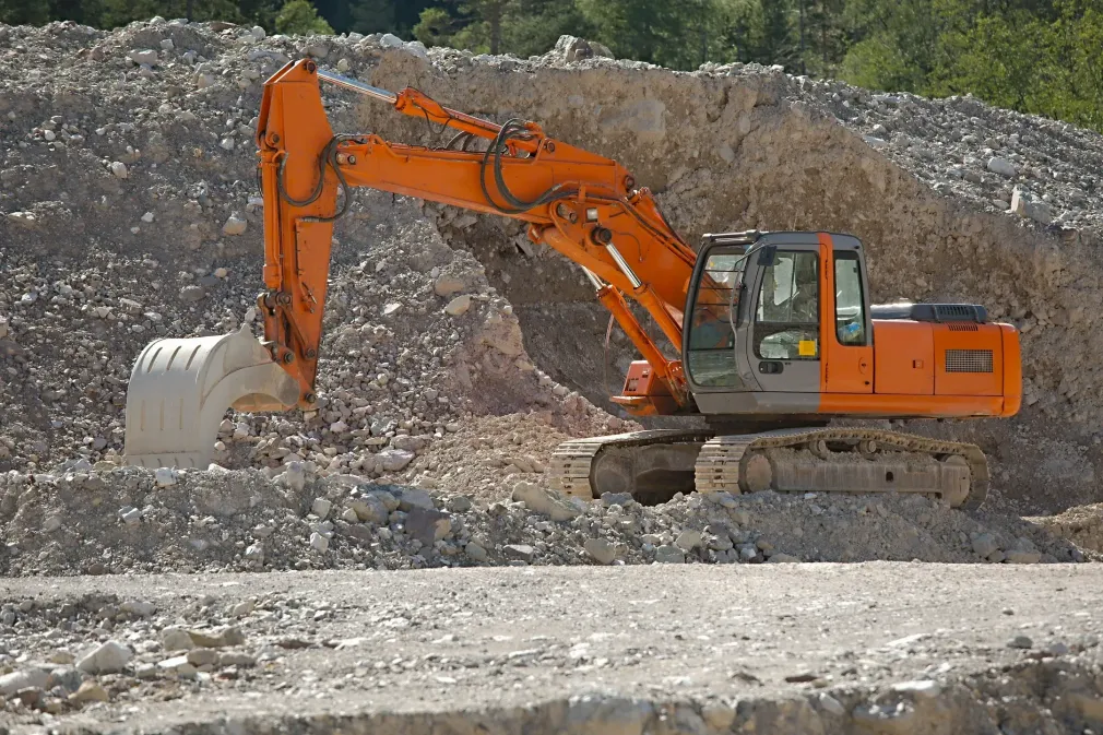 A large orange excavator is driving through a pile of rocks.