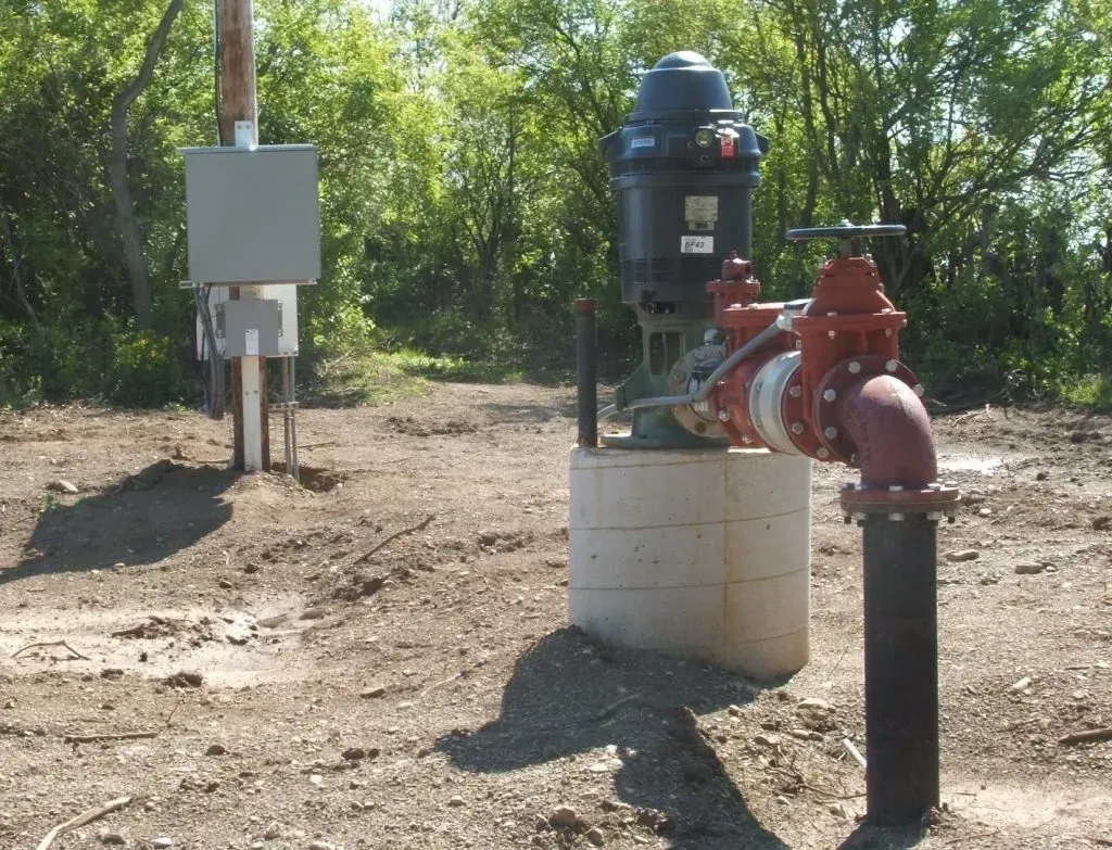 A water pump is sitting in the middle of a dirt field