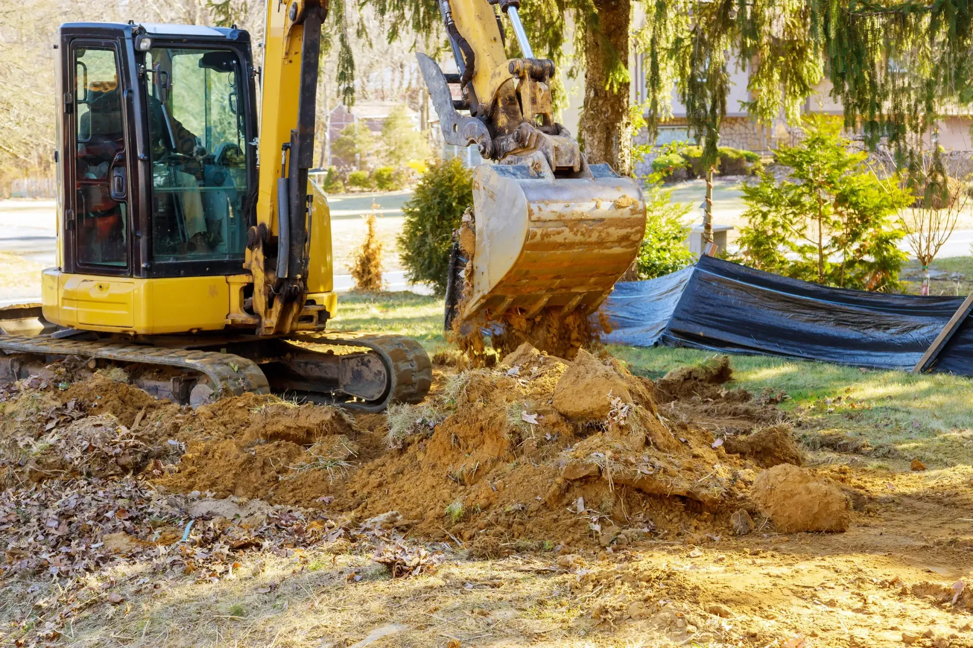 A yellow excavator is digging a hole in a yard.