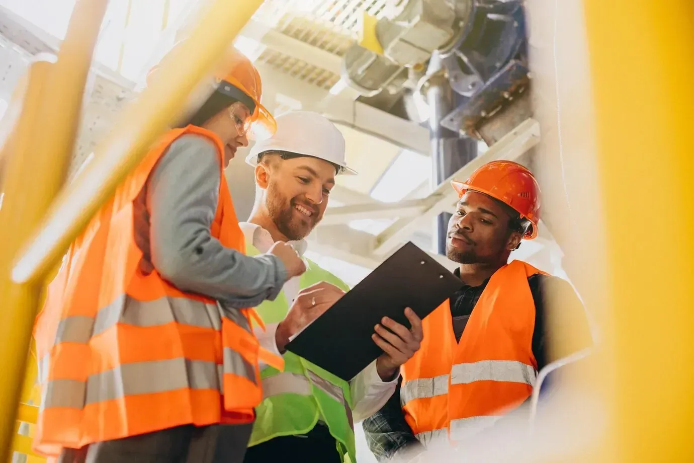 A group of construction workers are looking at a clipboard in a factory.