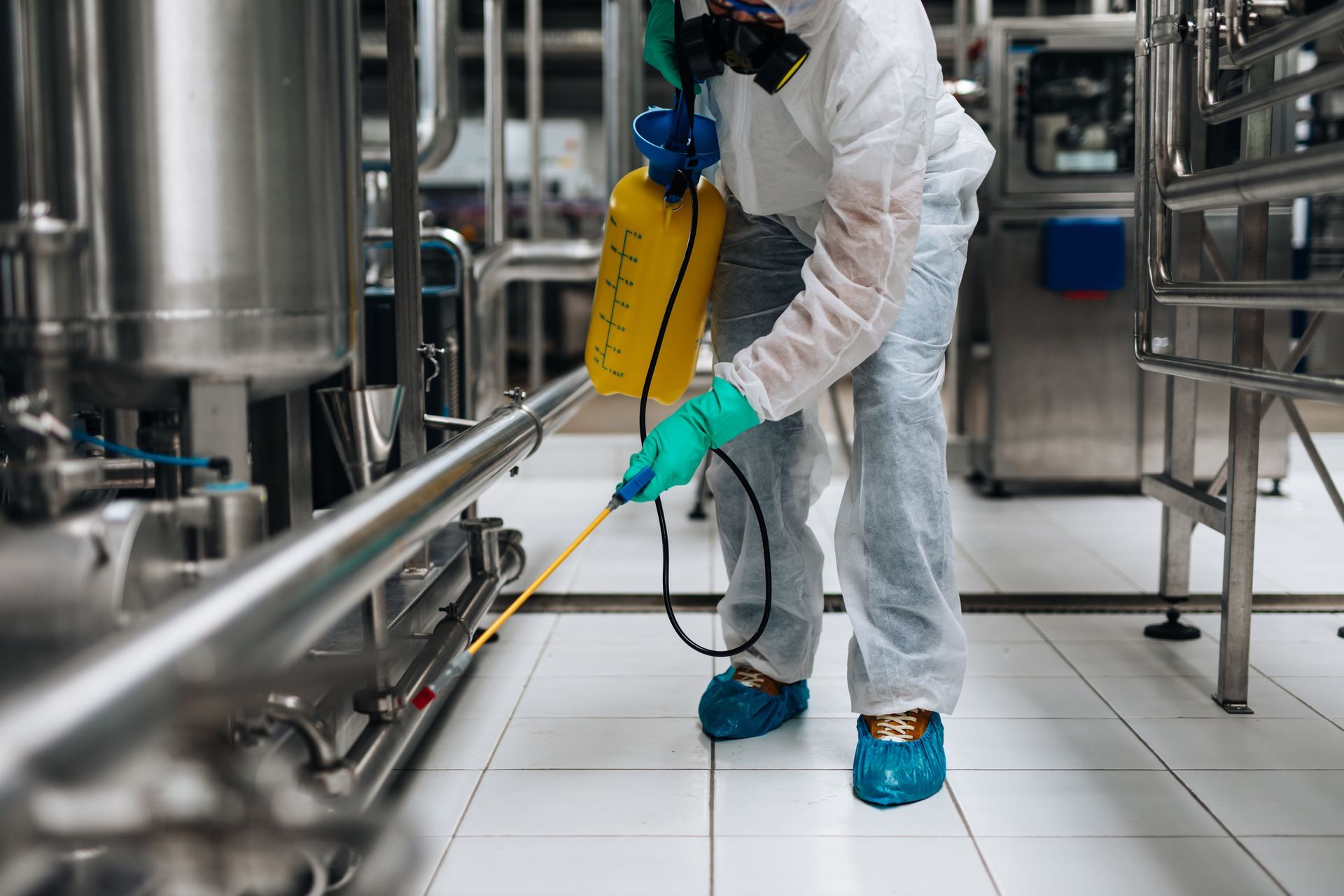 Person in protective suit spraying a cleaning solution in a stainless steel industrial facility.