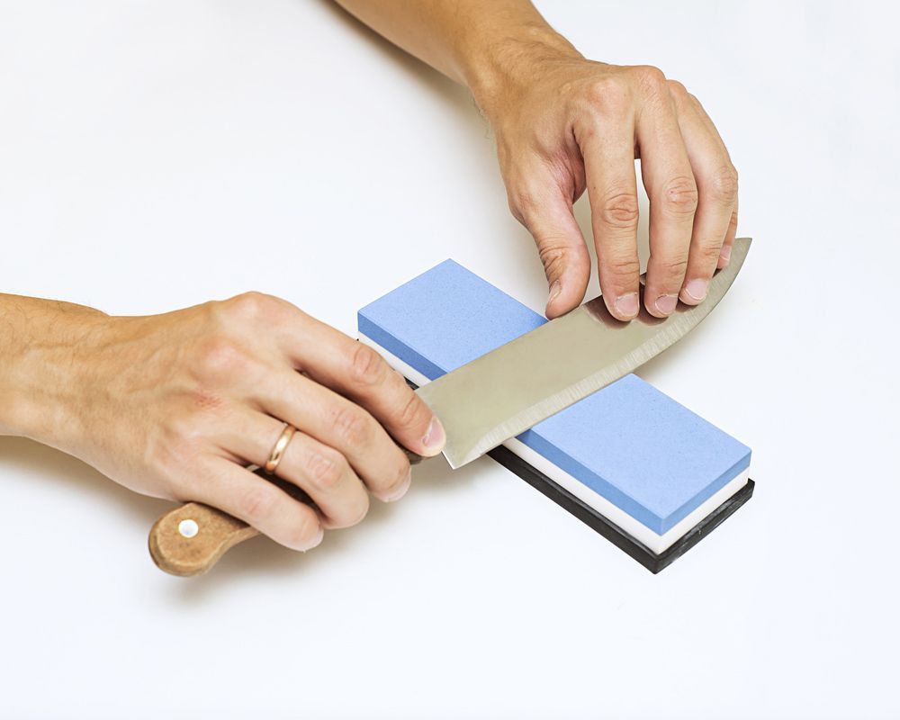 A Knife Being Sharpened With A Whetstone on a White Background — Shaving Sharp Knives And Tools in Toowoomba, QLD