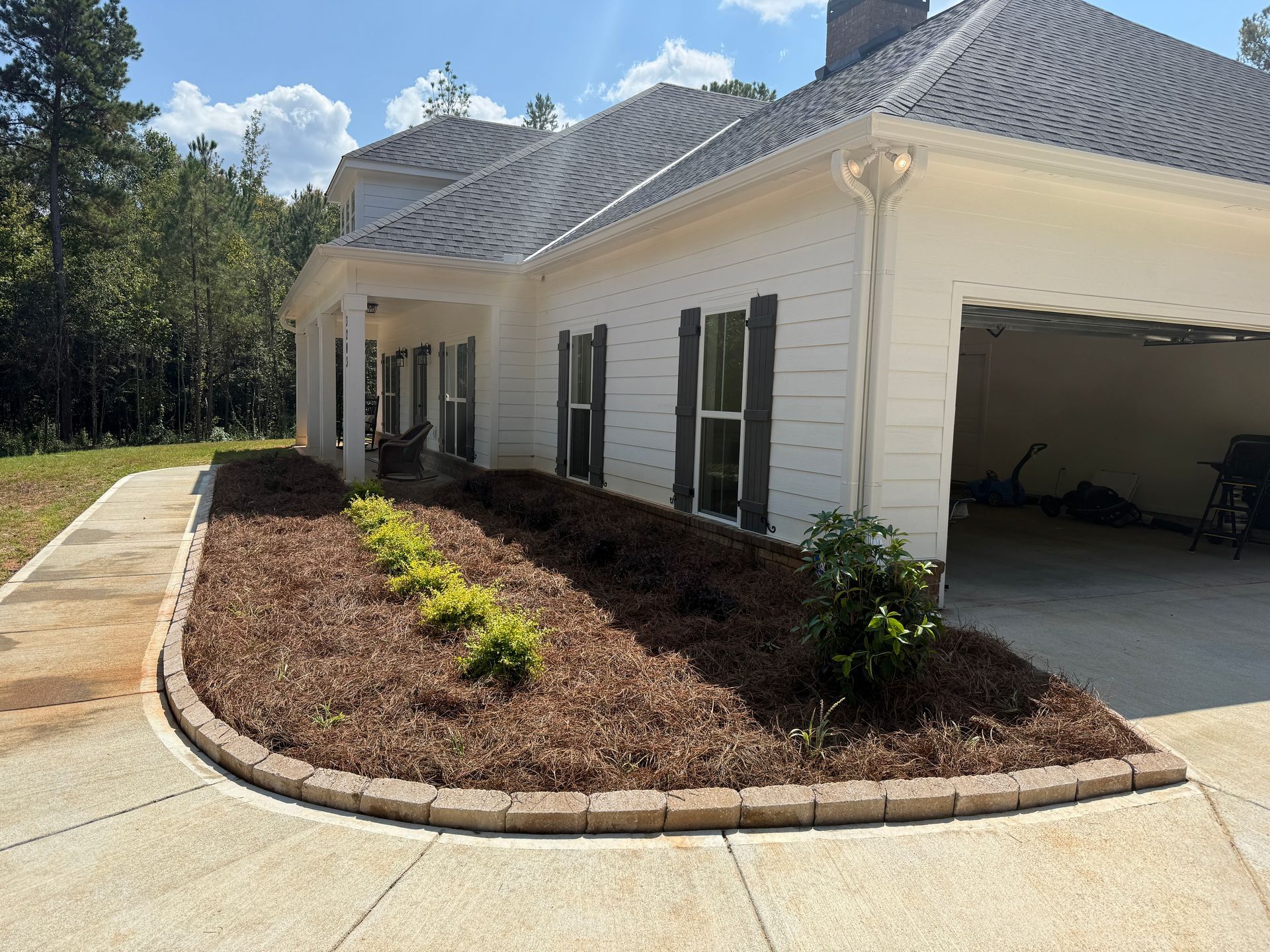 White house with dark shutters and a driveway with a landscaped bed edged in brick.