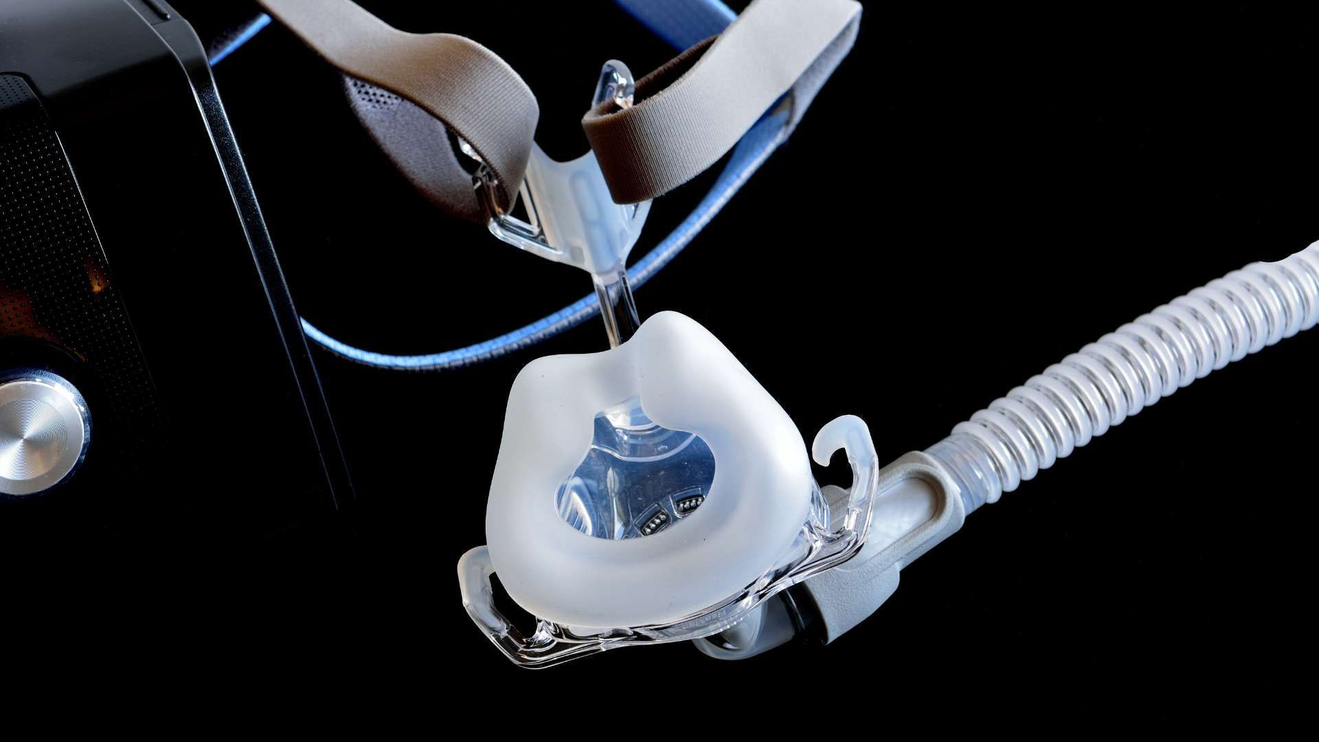 Close-up of a white oxygen mask with clear tubing and straps on a black background