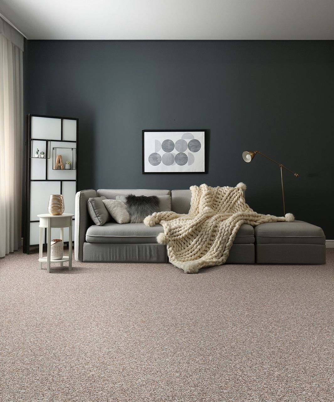 Living room with gray sofa, dark wall, neutral carpet, and beige chunky knit blanket.