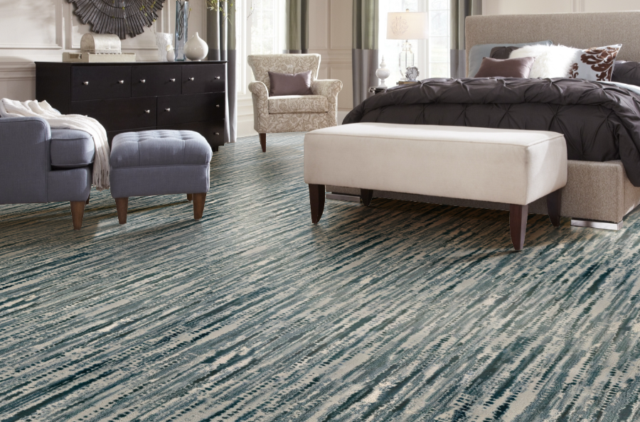 Bedroom with abstract blue and white patterned carpet, bed, seating, and dresser.