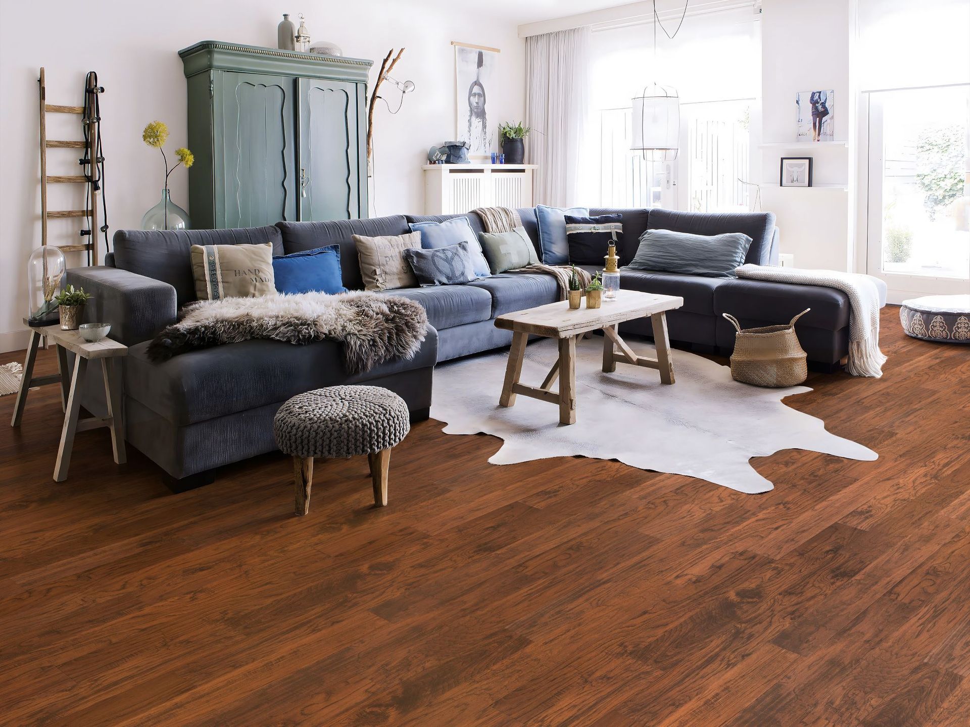 Living room with a large blue sectional, rustic coffee table, and wood flooring; rug and cabinet add interest.