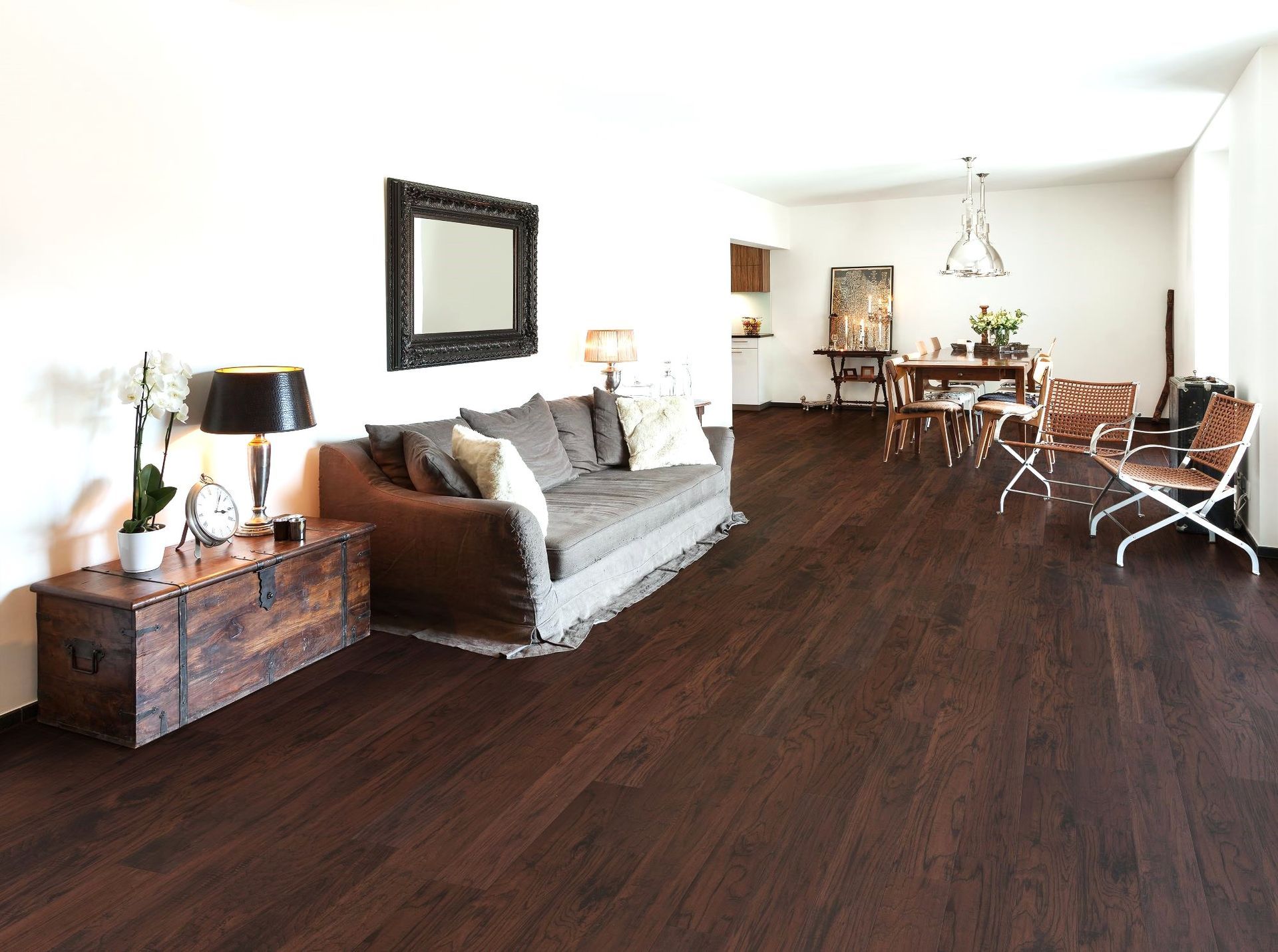 Living room with dark wood floors, couch, mirror, wooden chest, and dining table.