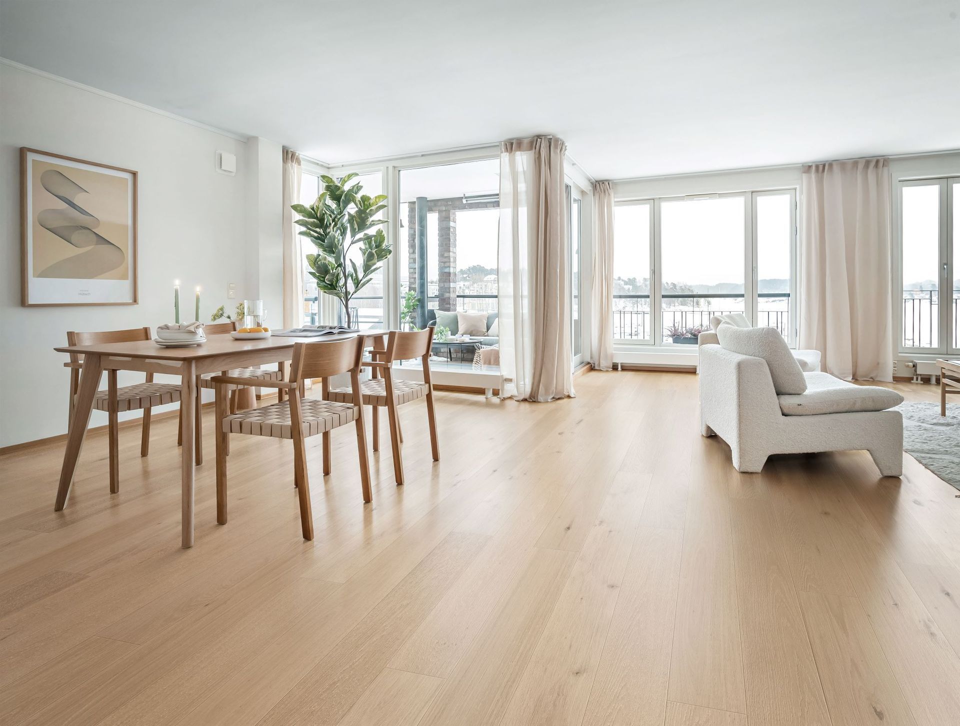 Bright living room with wooden floors, dining table, and large windows overlooking a balcony and water view.