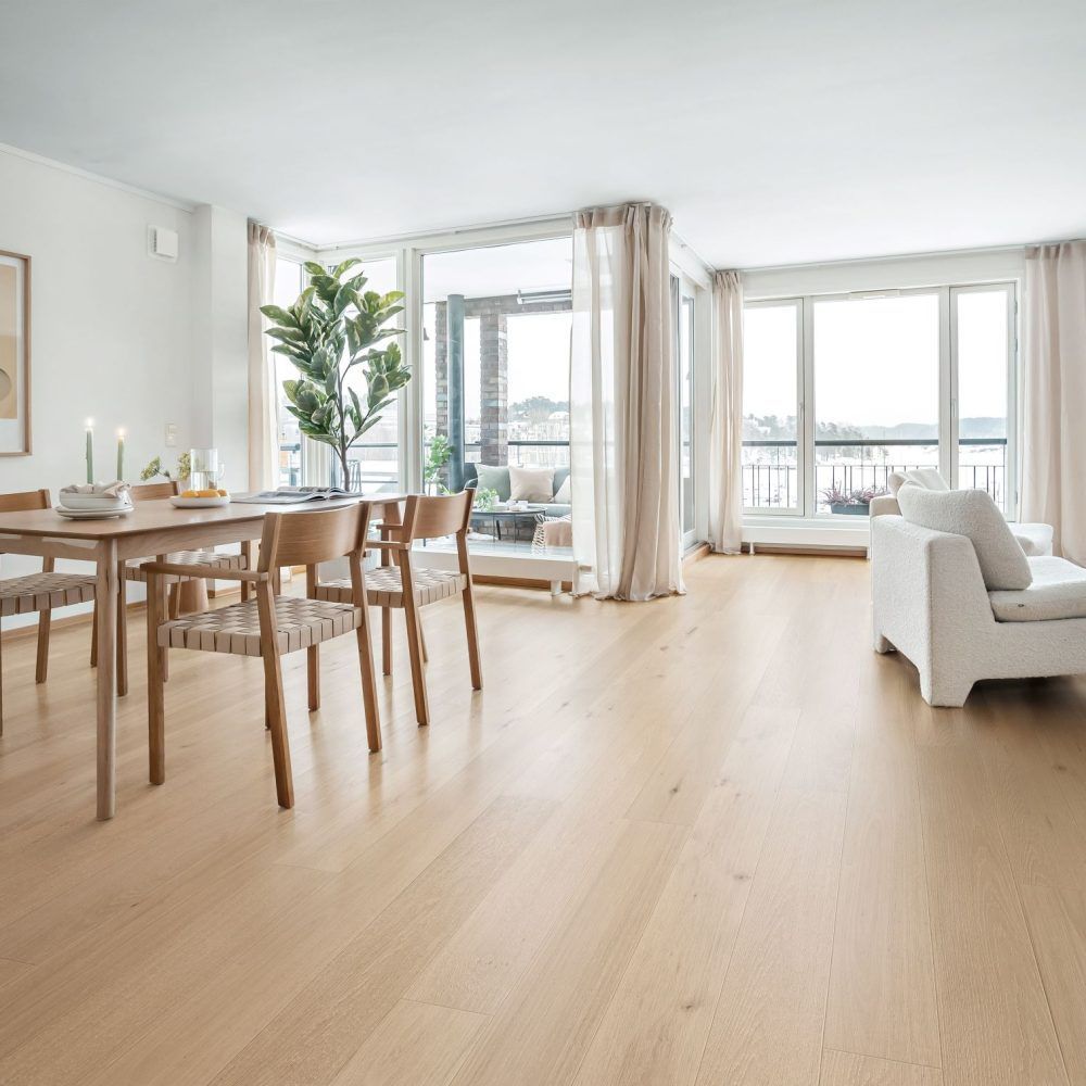 Light-filled living space with wooden floors, dining table, and white sofa near large windows with a view.