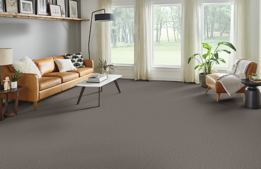 Living room with brown leather sofa, carpet, and large windows with a nature view.