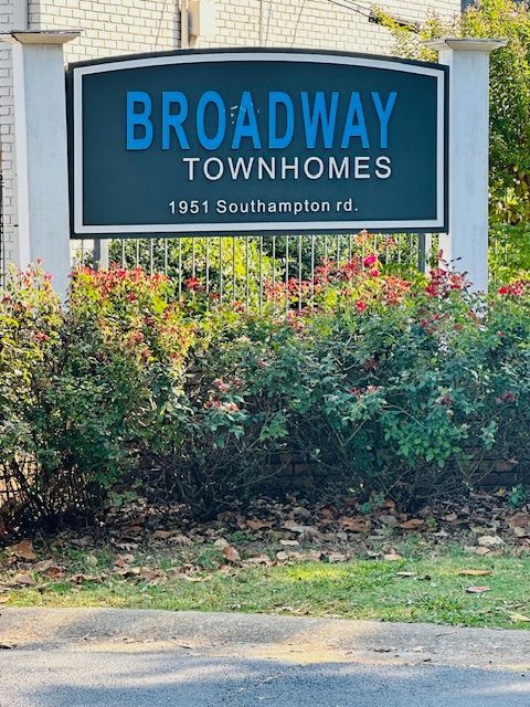 A sign for broadway townhomes sits in front of a bush