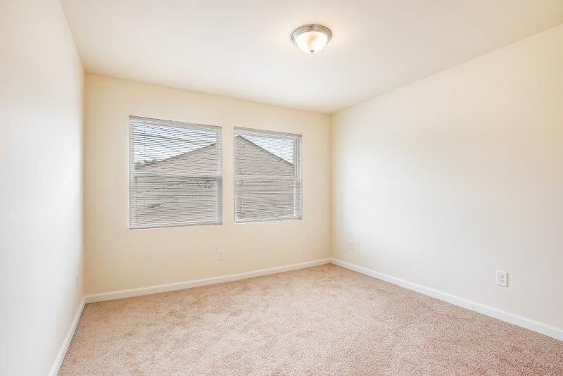 An empty bedroom with two windows and a carpeted floor.