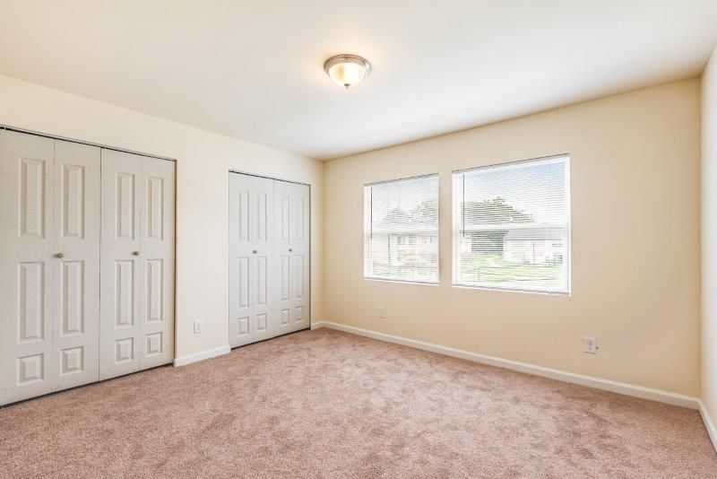 An empty bedroom with two closets and two windows.
