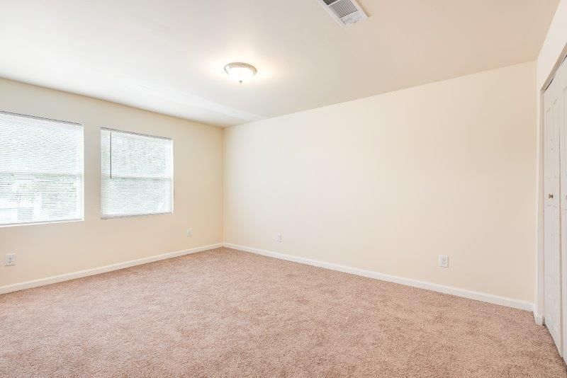 An empty bedroom with a carpeted floor and two windows.