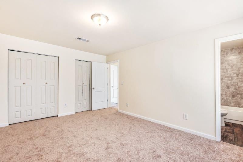 An empty bedroom with a carpeted floor and two closets.