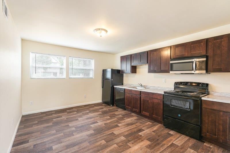 An empty kitchen with wooden floors and stainless steel appliances.