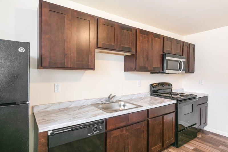 A kitchen with wooden cabinets , a black refrigerator , a stove , dishwasher , and microwave.
