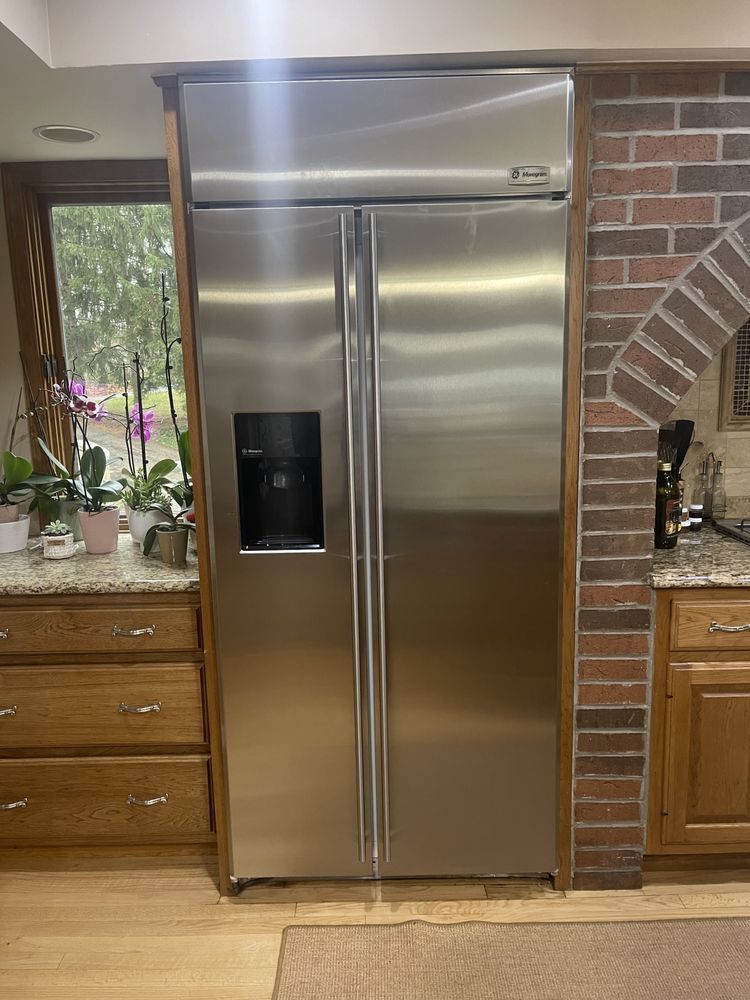 Stainless steel side-by-side refrigerator built into wooden cabinetry, with water dispenser.