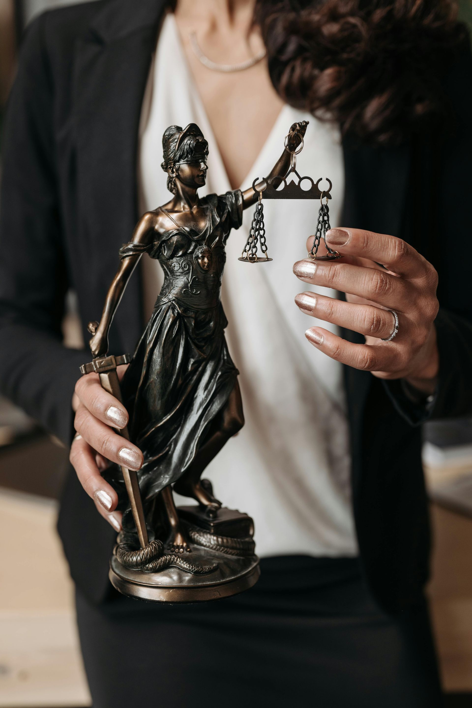 Woman in black suit holding a statue of Lady Justice, symbol of law.