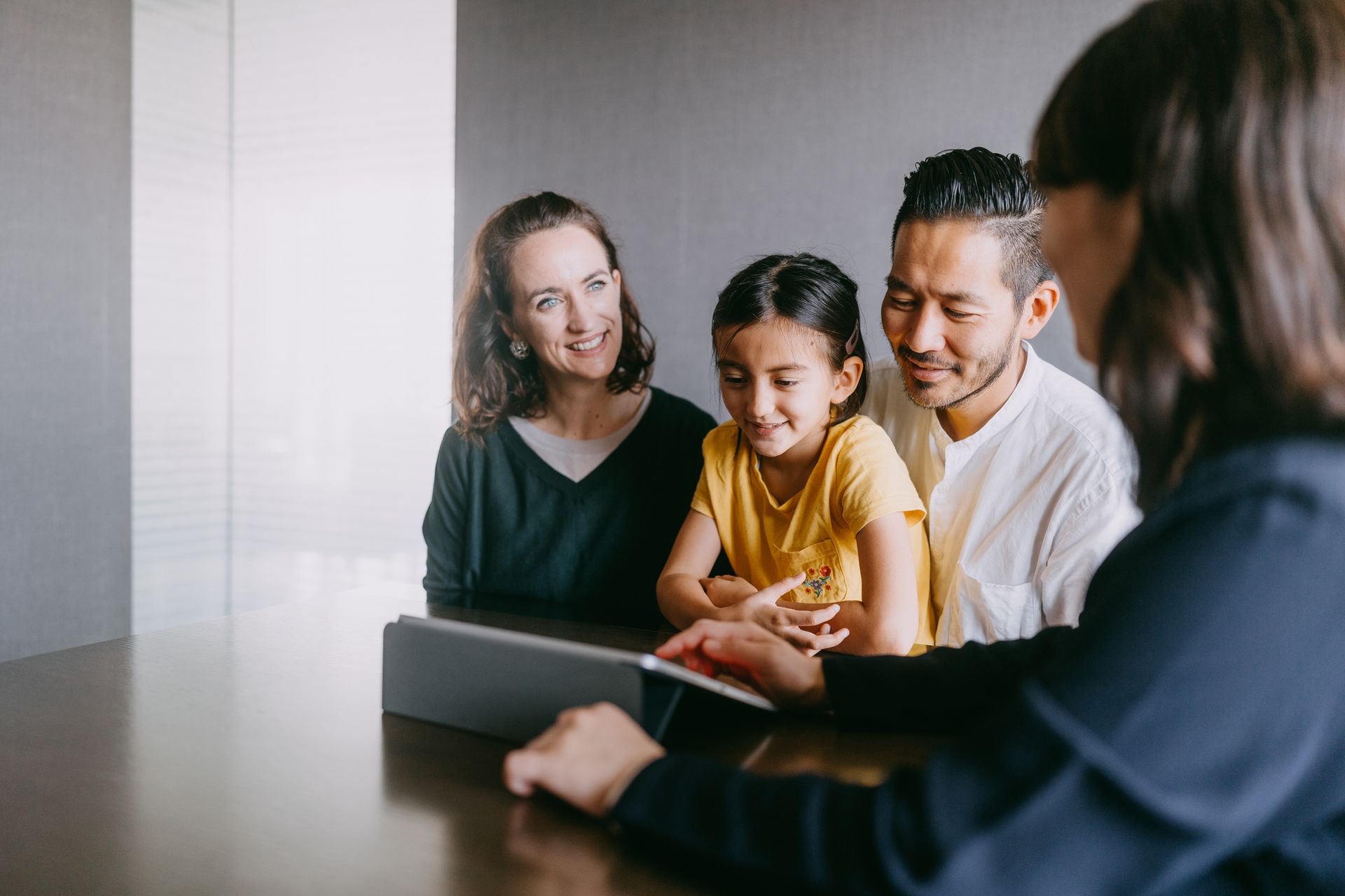 Family looking at a tablet with a professional, seated at a table in a modern setting.