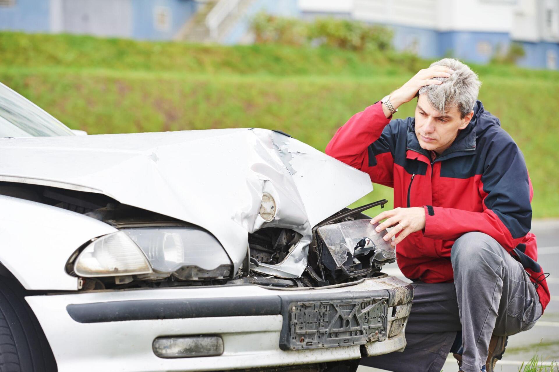 A man is kneeling down in front of a damaged car.