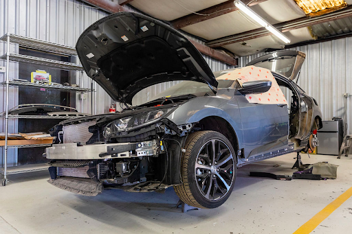 A car is being repaired in a garage with the hood open.