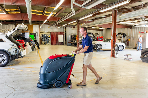 A man is cleaning the floor of a garage with a machine.