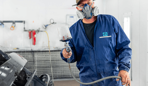 A man wearing a mask is spray painting a car in a garage.