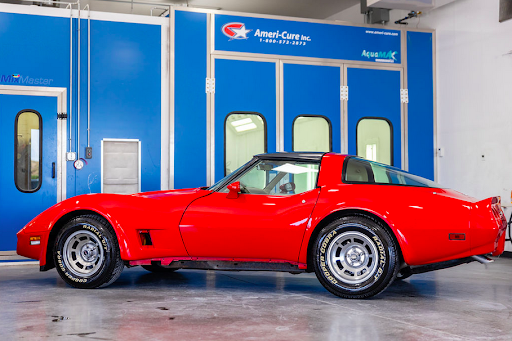 A red corvette is parked in front of a blue paint booth.