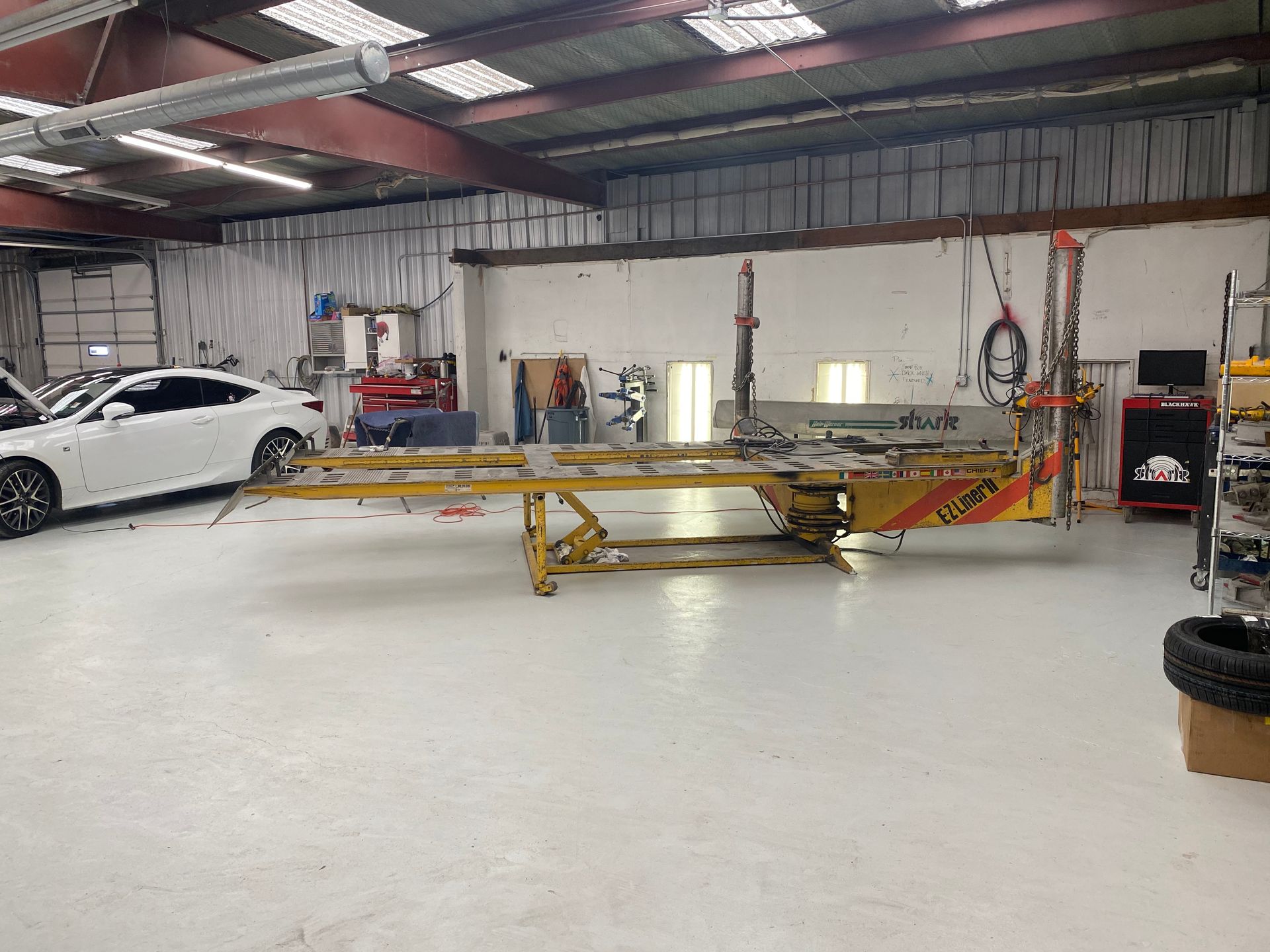 A white car is parked in a garage next to a yellow lift.